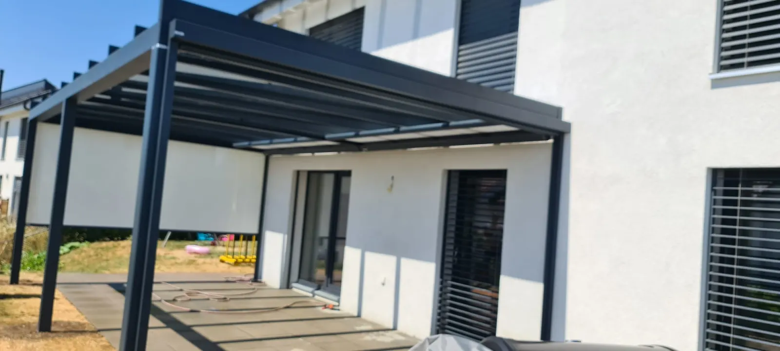Structure aluminium devant une terrasse, avec protection solaire intégrée et stores à lamelles visibles sur la façade.