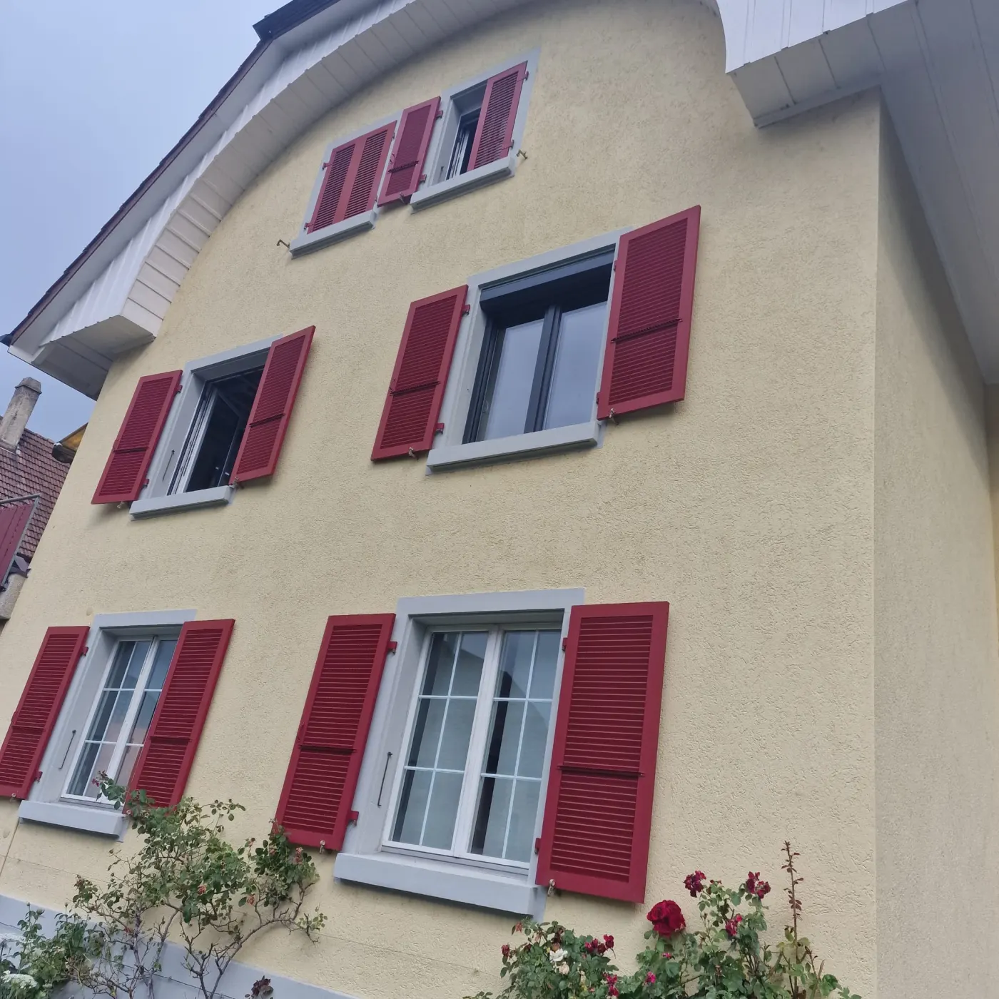 Façade résidentielle équipée de volets battants rouges sur plusieurs fenêtres.